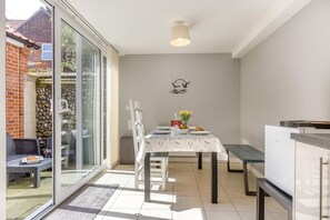 A dining area with a table set for two, a bench, and a view through a glass door to an outdoor patio. - 2 Bed in Cromer (oc-90187) (Cromer)