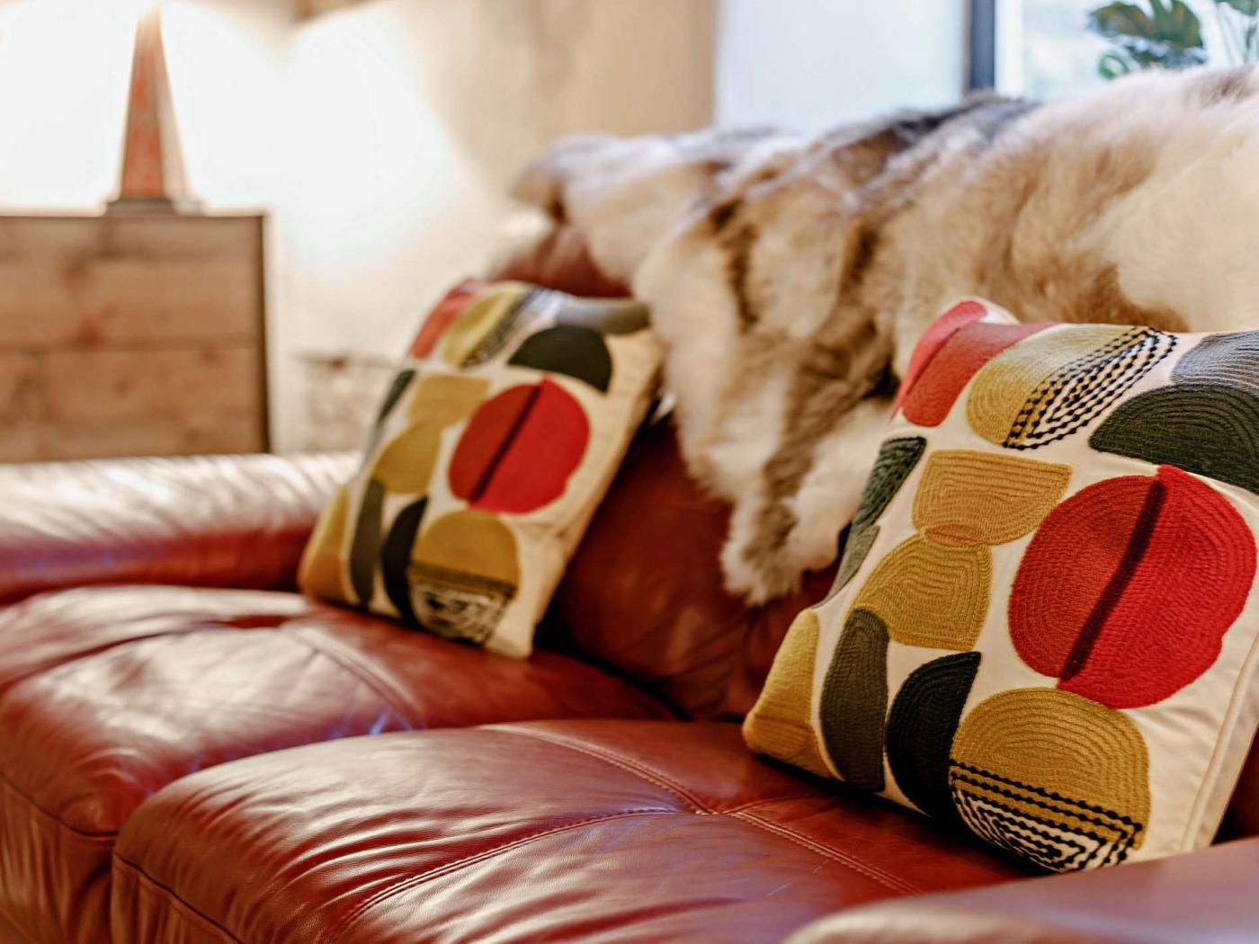 A leather sofa with patterned cushions and a fur throw.