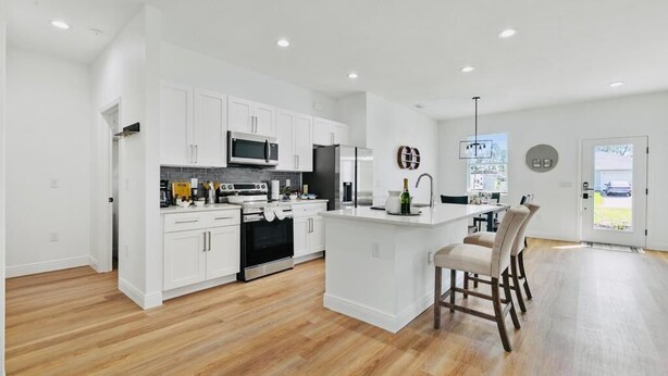 A modern kitchen with white cabinetry, a central island, and a dining area with bar stools.