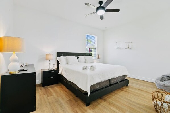 A bedroom with a bed, bedside tables, a ceiling fan, a window, and a wall-mounted light fixture.