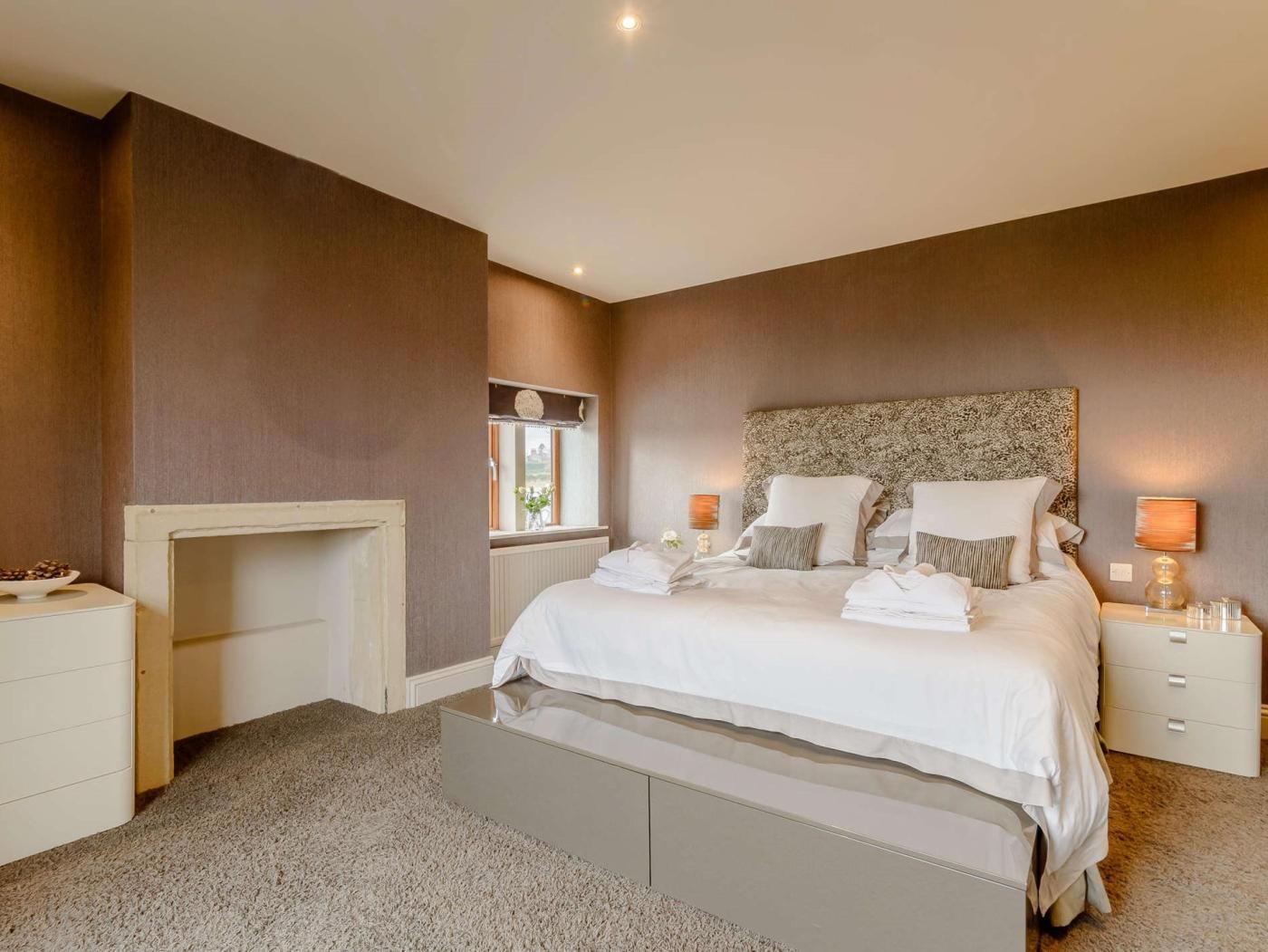 A bedroom with a bed, bedside tables, a nightstand, a window, and a fireplace.