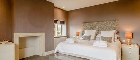 A bedroom with a bed, bedside tables, a nightstand, a window, and a fireplace.