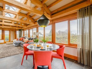 A spacious room with a high ceiling, a round dining table with chairs, a sofa, and large windows offering a view of the outdoors. - 3 Bed in Halifax (oc-90209) (Sowerby Bridge)