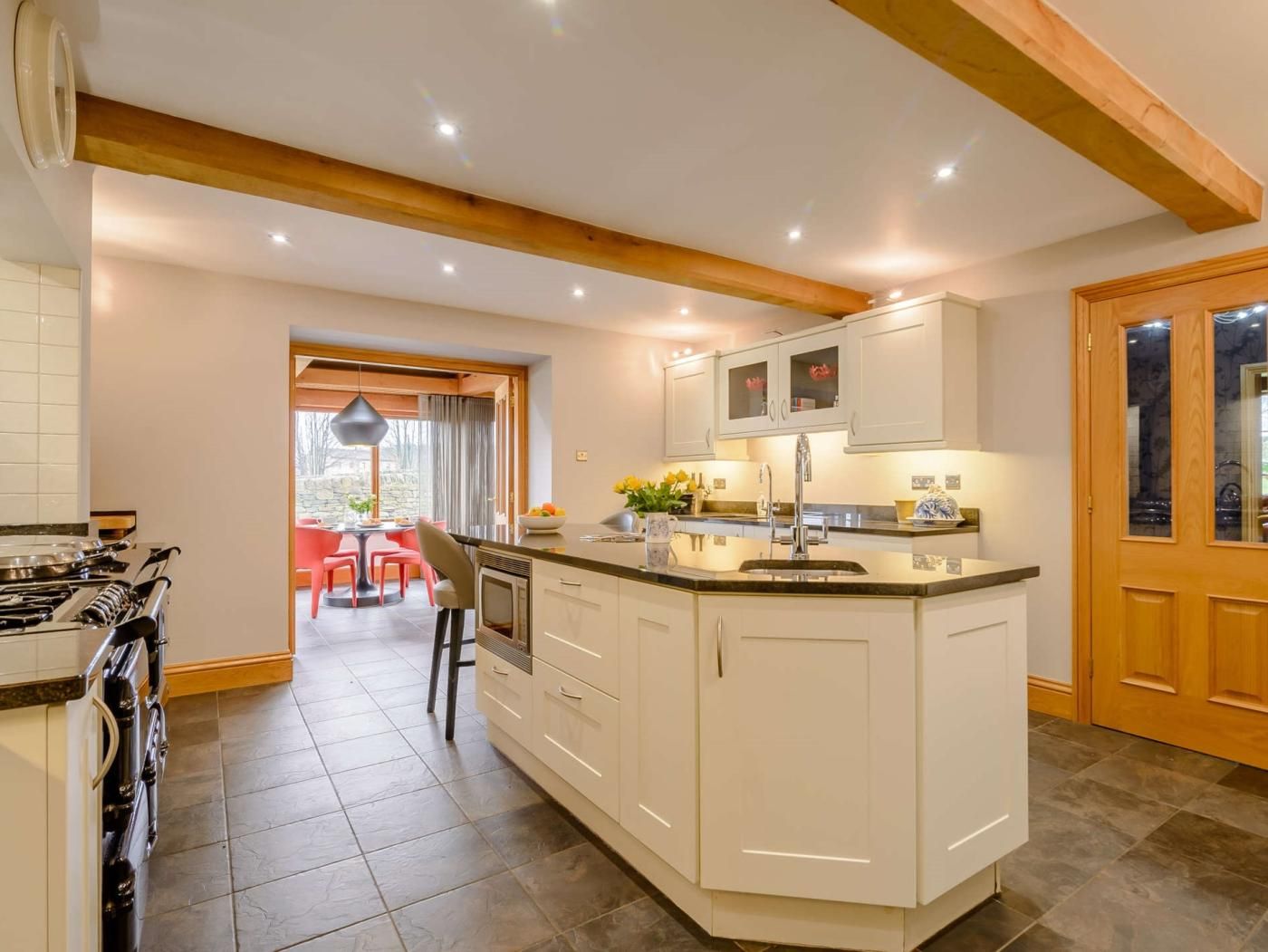 A modern kitchen with white cabinetry, a central island, and a dining area with red chairs.