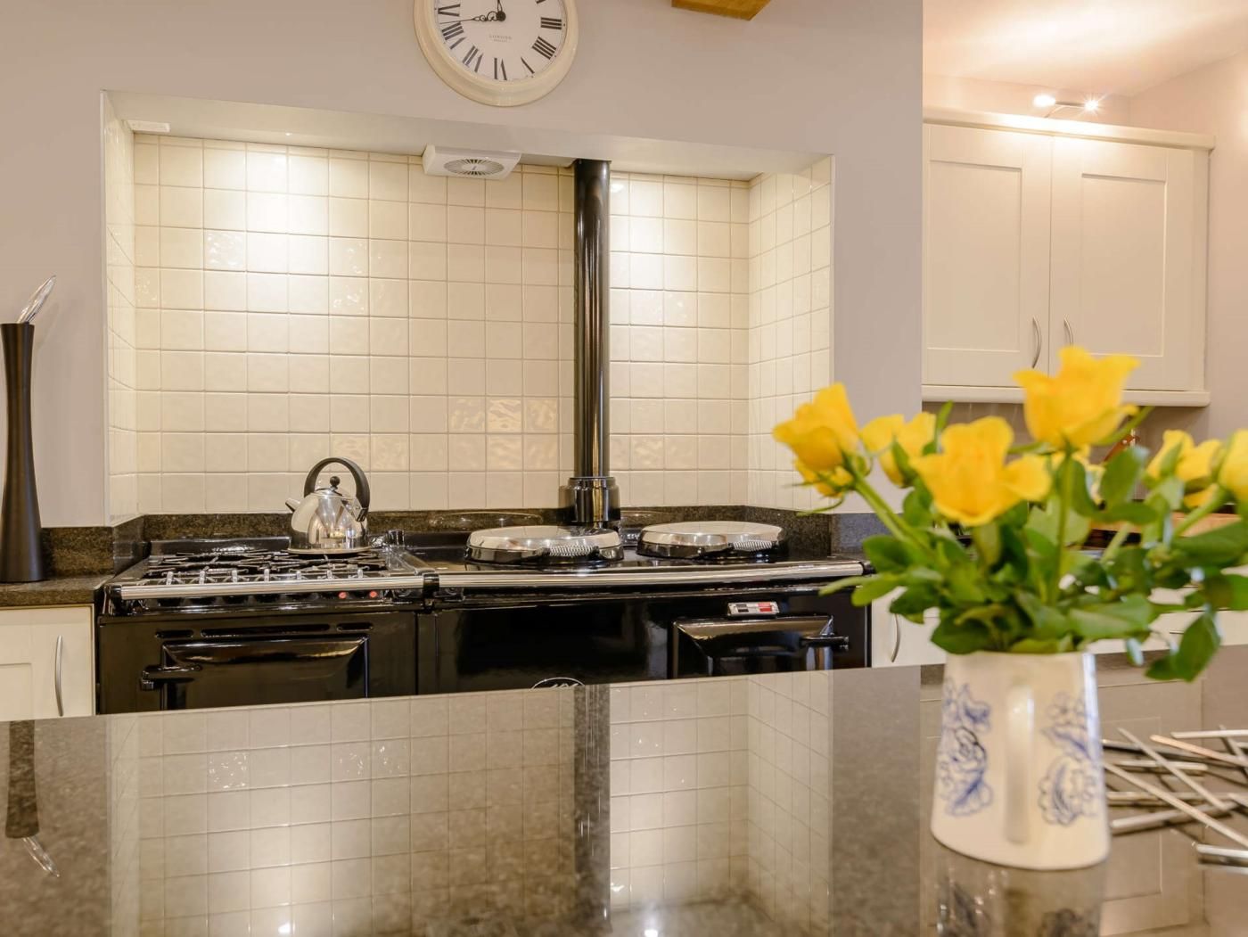 A kitchen with a stove, a clock, and a vase with flowers on the counter.