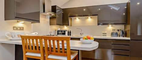 Una cocina moderna con comedor, que incluye una mesa de madera, un cuenco de fruta y electrodomésticos de acero inoxidable.