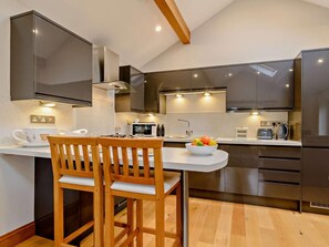 Una cocina moderna con comedor, que incluye una mesa de madera, un cuenco de fruta y electrodomésticos de acero inoxidable.