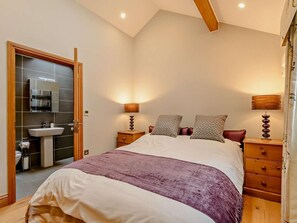Un dormitorio con cama, mesitas de noche, cómoda, espejo y baño con lavamanos e inodoro.