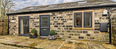 A stone building with a dark door, windows, and a small garden area with potted plants.