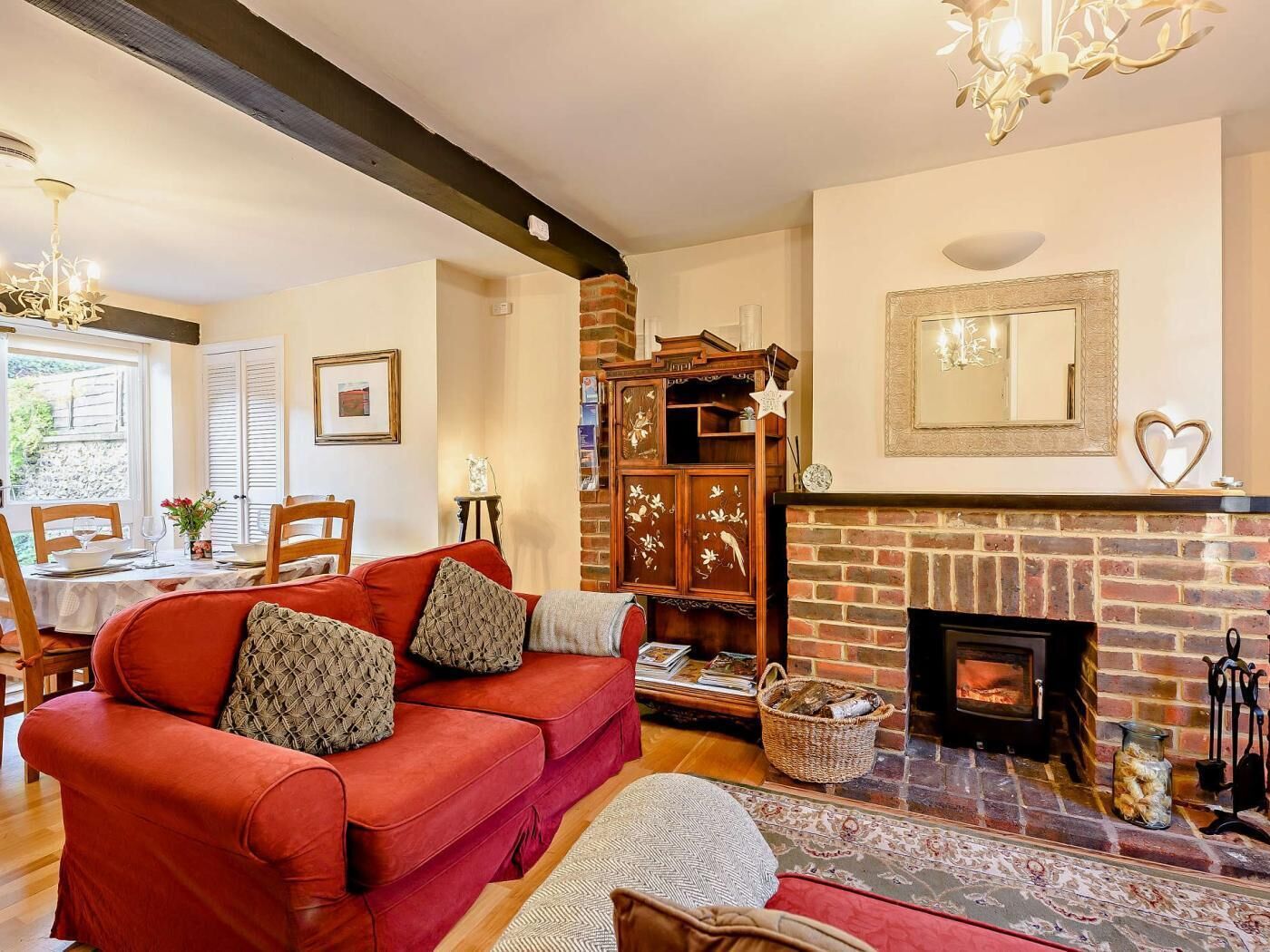 A cozy living room with a red sofa, fireplace, wooden cabinet, and a dining area with a table and chairs.
