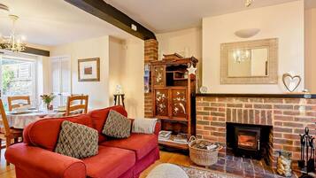 A cozy living room with a red sofa, fireplace, wooden cabinet, and a dining area with a table and chairs.
