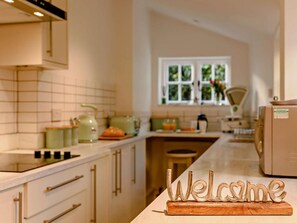 A kitchen with a 'Welcome' sign, a window with a view of greenery, and a countertop with various kitchen items. - 2 Bed in Arundel (oc-89671) (Arundel)