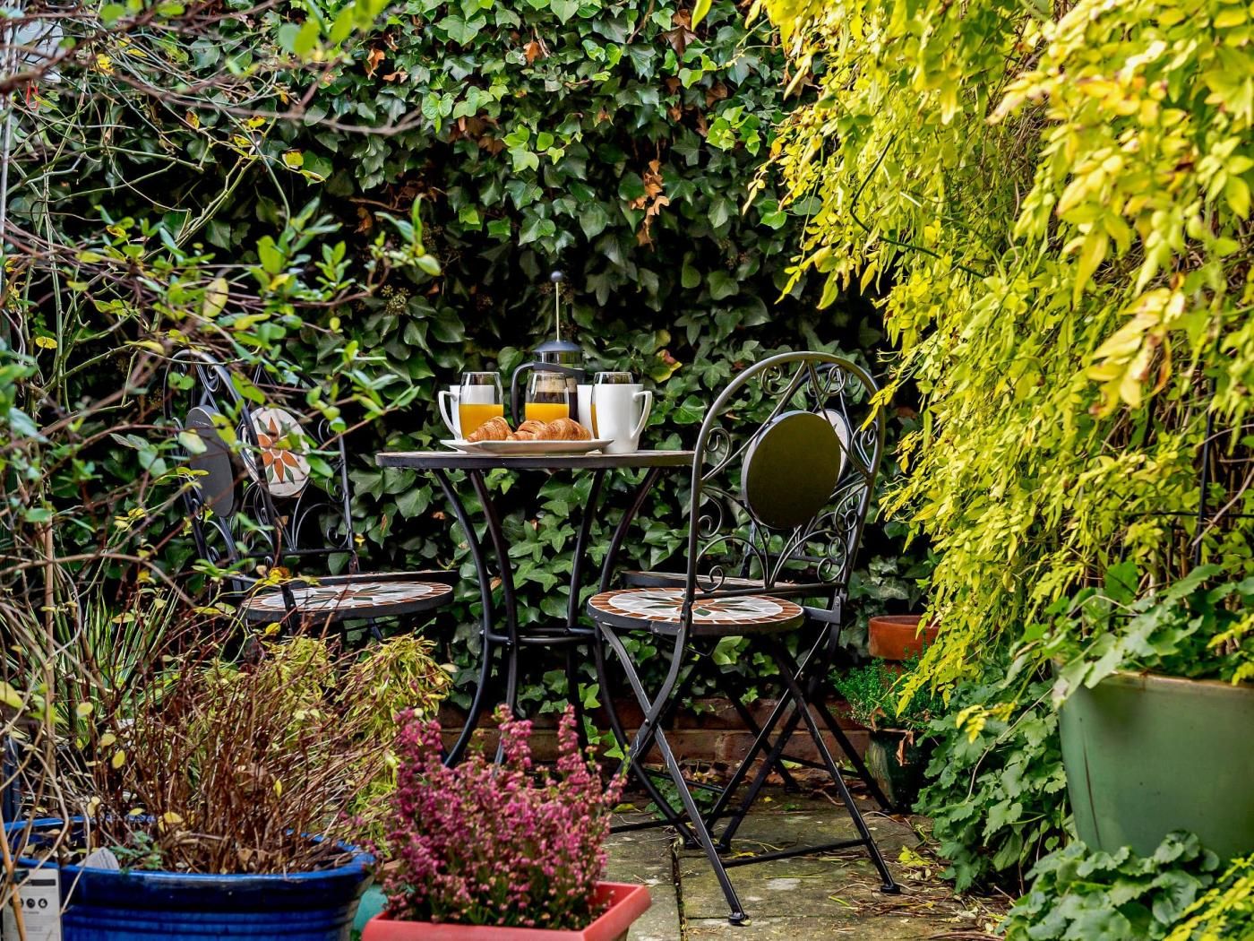 An outdoor seating area with a table and chairs, surrounded by lush greenery and potted plants.