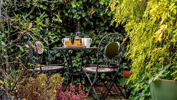 An outdoor seating area with a table and chairs, surrounded by lush greenery and potted plants.