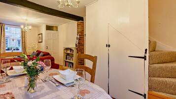 A dining area with a table set for four, a vase of flowers, and a bookshelf in the background.