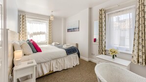 Une chambre à coucher avec un lit, une table de chevet, une lampe, une chaise et une fenêtre avec des rideaux.