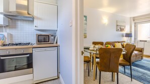 Une cuisine compacte équipée d’un four à micro-ondes, d’une cuisinière et d’un lave-vaisselle. À côté se trouve un coin repas avec une table, des chaises et un canapé.