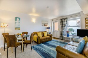 A living room with a sofa, chairs, a coffee table, a TV, and a window with curtains. - 1 Bed in Aldeburgh (oc-89682) (Aldeburgh)