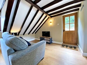 Ein Loft-Zimmer mit freiliegenden Holzbalken, einem Fernseher auf einem Standfuß, einer Couch und einer Holztür.