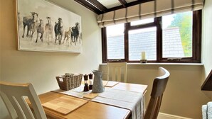 Un comedor con una mesa de madera, sillas, un cuadro de caballos y una ventana con vistas.