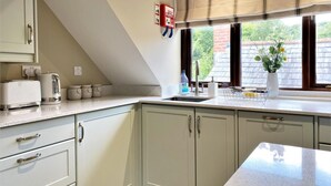 Una cocina con armarios blancos, una encimera, un hervidor, un tostador, un lavabo y una ventana con vistas a zonas verdes.