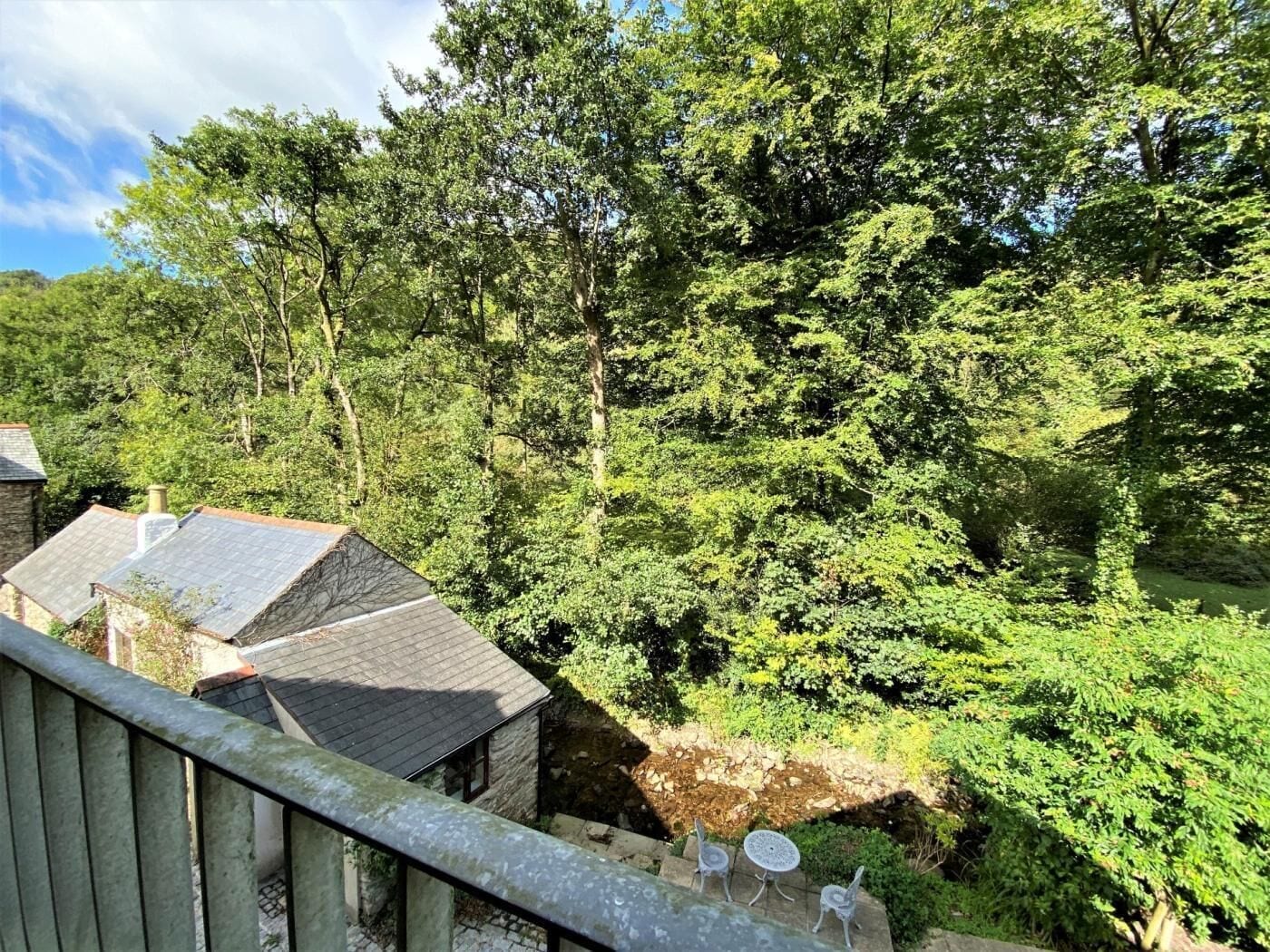 A stone building with a sloped roof, surrounded by dense green foliage.