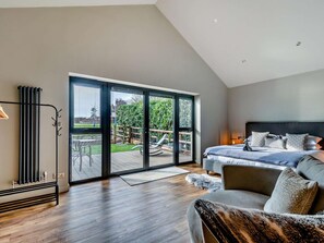 Ein modernes Schlafzimmer mit einem großen Bett, Blick auf einen Garten durch eine Glastür und einem Heizkörper an der Wand.