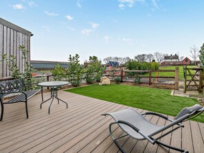 Eine Holzterrasse mit Tisch und Stühlen, eine Rasenfläche und ein Spielplatz im Hintergrund.
