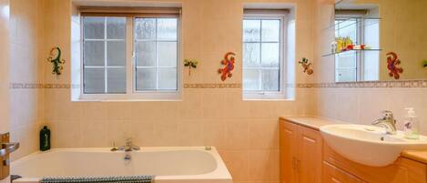 A bathroom with a bathtub, a sink, and two windows.