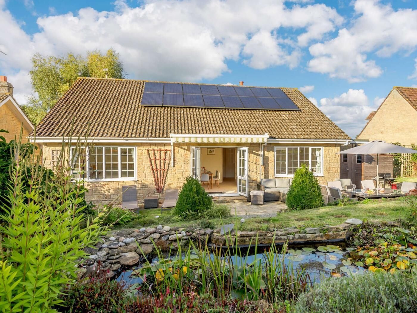 A house with a tiled roof, a garden with a pond, and solar panels.