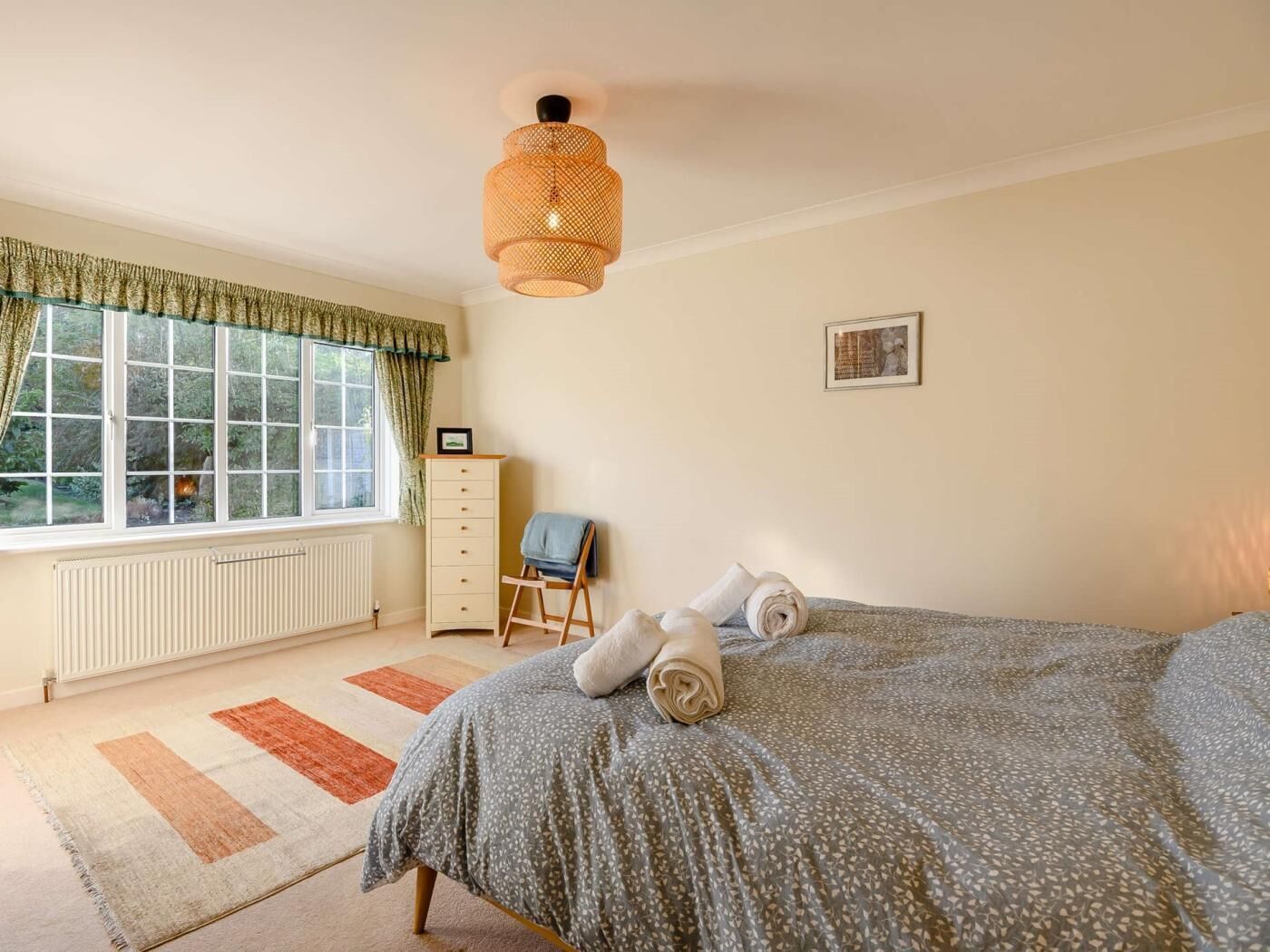 A bedroom with a bed, a dresser, a chair, a radiator, and a window with curtains.