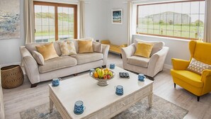 A living room with a beige sofa, a yellow armchair, and a coffee table with fruit and cups. - 4 Bed in Bideford (oc-89870) (Westward Ho!)