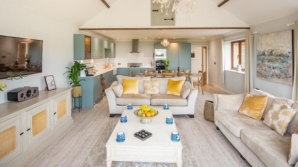 A spacious living area with a high ceiling, a chandelier, a dining area, and a kitchen. - 4 Bed in Bideford (oc-89870) (Westward Ho!)