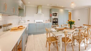 A modern kitchen with light blue cabinets, stainless steel appliances, and a dining area with wooden chairs and a table set for four. - 4 Bed in Bideford (oc-89870) (Westward Ho!)