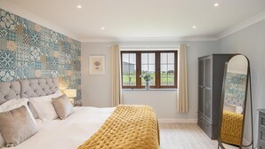 A bedroom with a large bed, a window with a view of a field, a mirror, and a wardrobe. - 4 Bed in Bideford (oc-89870) (Westward Ho!)