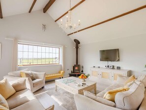 Ein geräumiges Wohnzimmer mit hoher Decke, Kamin, Fernseher und einem großen Fenster mit Blick ins Freie.