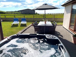 A hot tub with a view of a backyard patio area, including a table and chairs, and a wooden fence in the background. - 4 Bed in Bideford (oc-89870) (Westward Ho!)