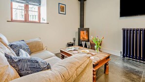 En hyggelig stue med sofa, sofabord i træ, pejs, et vindue og en radiator.