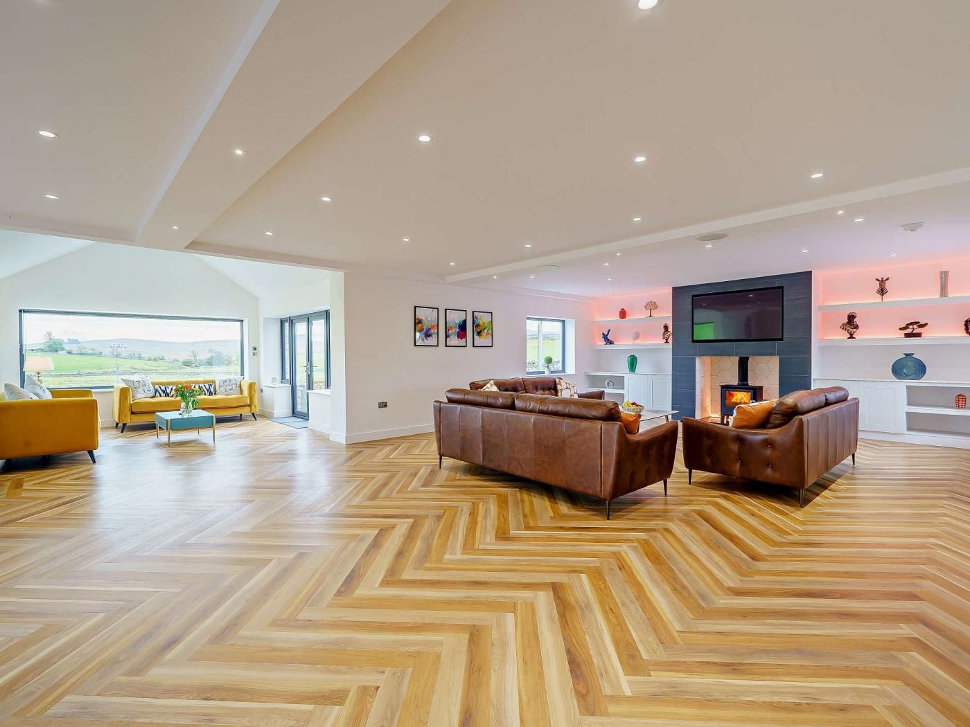 A spacious living room with a herringbone floor pattern, a fireplace, and a large TV mounted on the wall.
