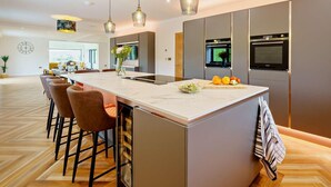 Una cocina moderna con una isla grande, taburetes de bar, iluminación colgante, hornos empotrados y vistas al área de comedor.