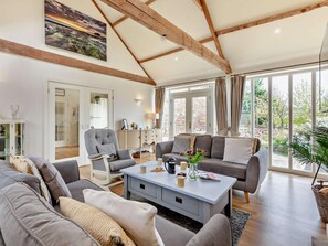 Ein geräumiges Wohnzimmer mit hoher Decke, großen Fenstern und Blick ins Freie.