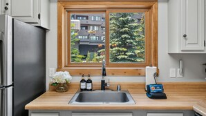 A kitchen with a stainless steel refrigerator, a wooden countertop, a sink, and a window with a view of buildings and trees. - Cedars Retreat - Walk to Main St & Trails & Pool (Breckenridge)
