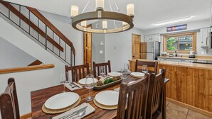 A dining area with a wooden table set for six, a chandelier, and a kitchen in the background. - Cedars Retreat - Walk to Main St & Trails & Pool (Breckenridge)