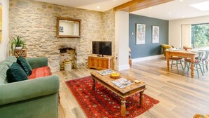 Un salon avec un mur en pierre, une cheminée, un téléviseur, un coin repas avec une table et des chaises, et un tapis rouge.