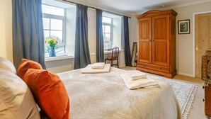 Une chambre à coucher avec un lit, une armoire en bois, une fenêtre avec des rideaux et un luminaire suspendu.