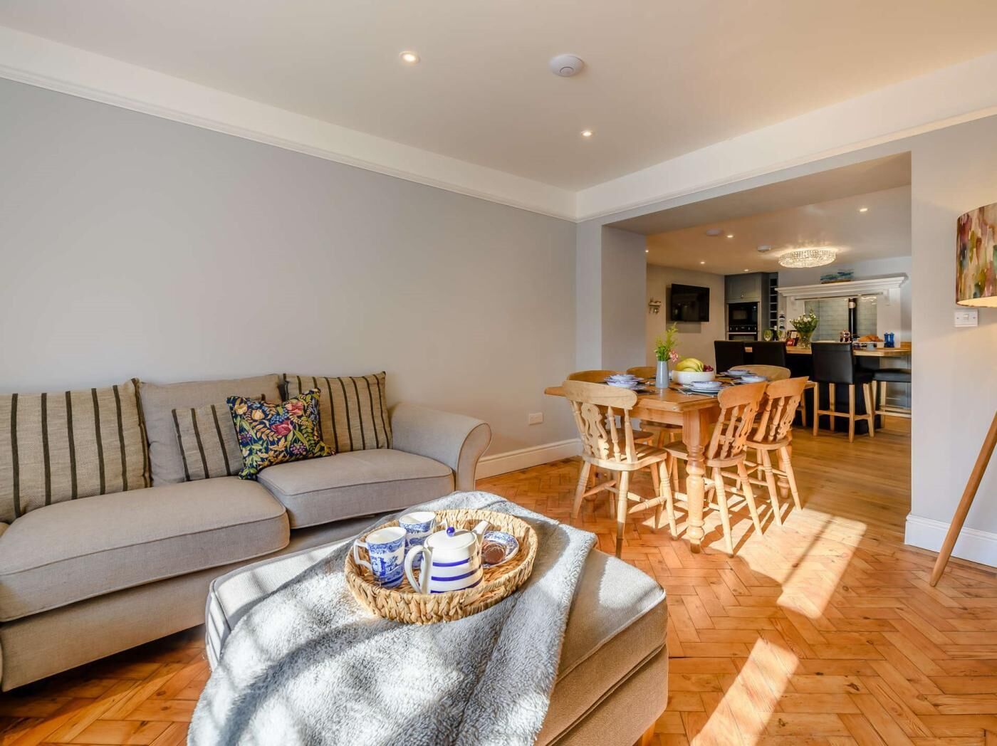 A living room with a sofa, a coffee table with a tray, and a dining area with wooden chairs and a table.