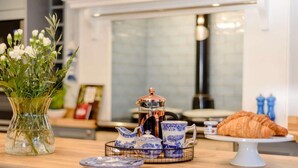 Een ontbijttafel met een koffiezetapparaat, een croissant en een bloevas.