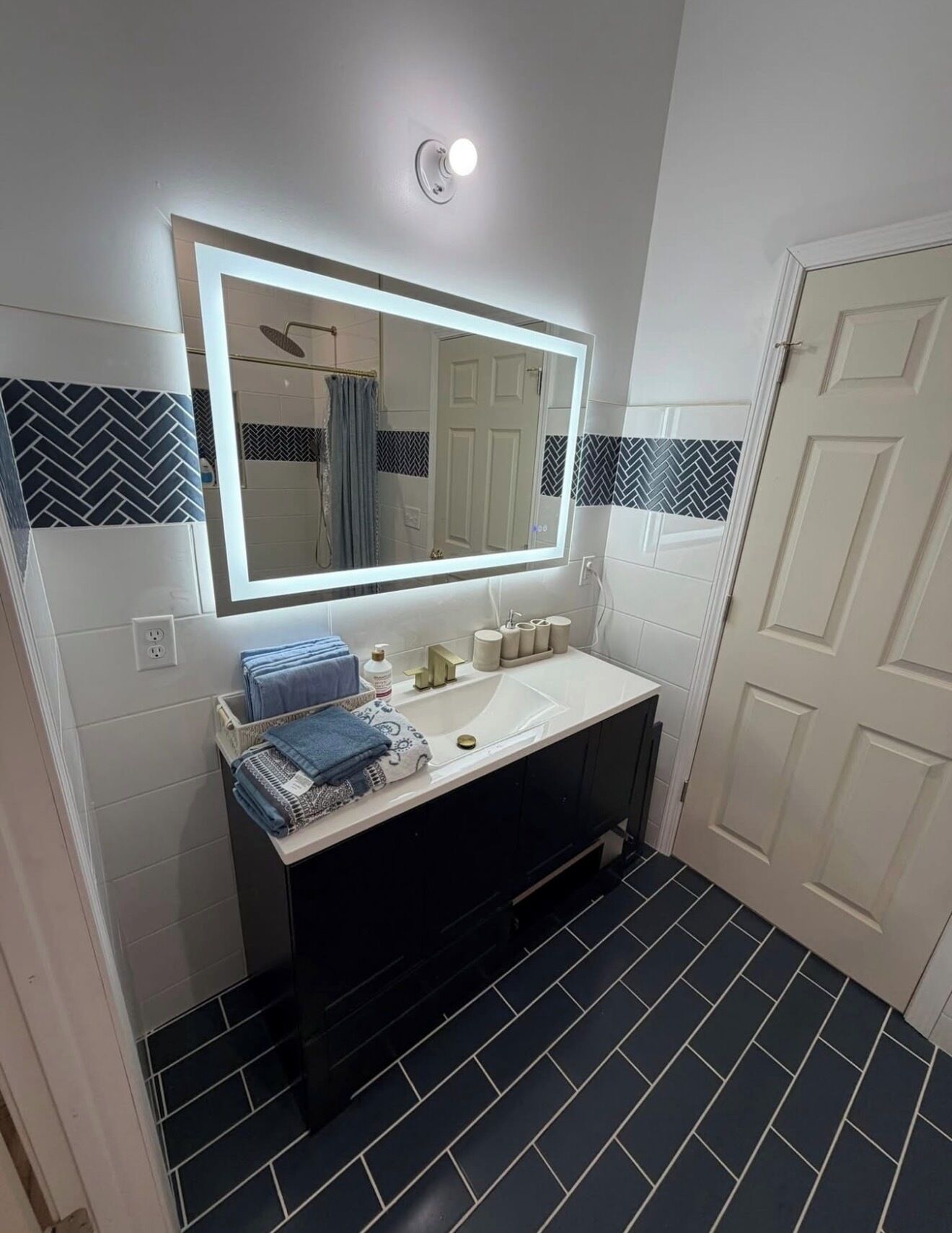 A bathroom with a large mirror, white sink, black tiles, and a towel rack.