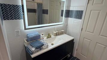 A bathroom with a large mirror, white sink, black tiles, and a towel rack.