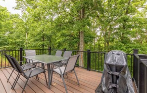 Une terrasse dotée d’une table et de chaises, entourée d’une rambarde noire, et un barbecue recouvert d’une bâche de protection.